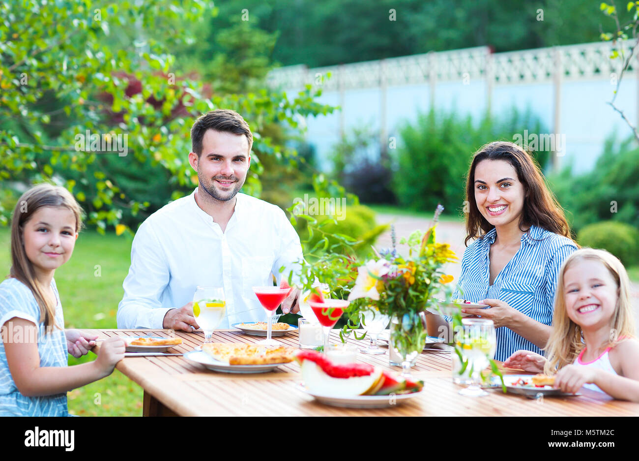 La famiglia felice di quattro persone godendo di pasto insieme mentre è seduto al tavolo da pranzo all'aperto Foto Stock