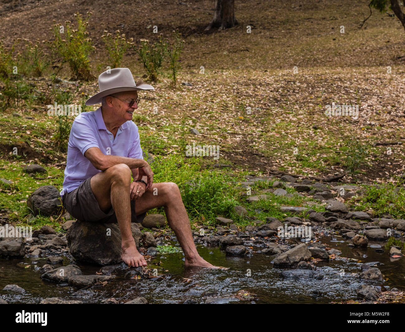 Anziani uomo Australiano, indossando un stetson, seduta da un torrente in alto la Hunter Valley, NSW, Australia. Foto Stock