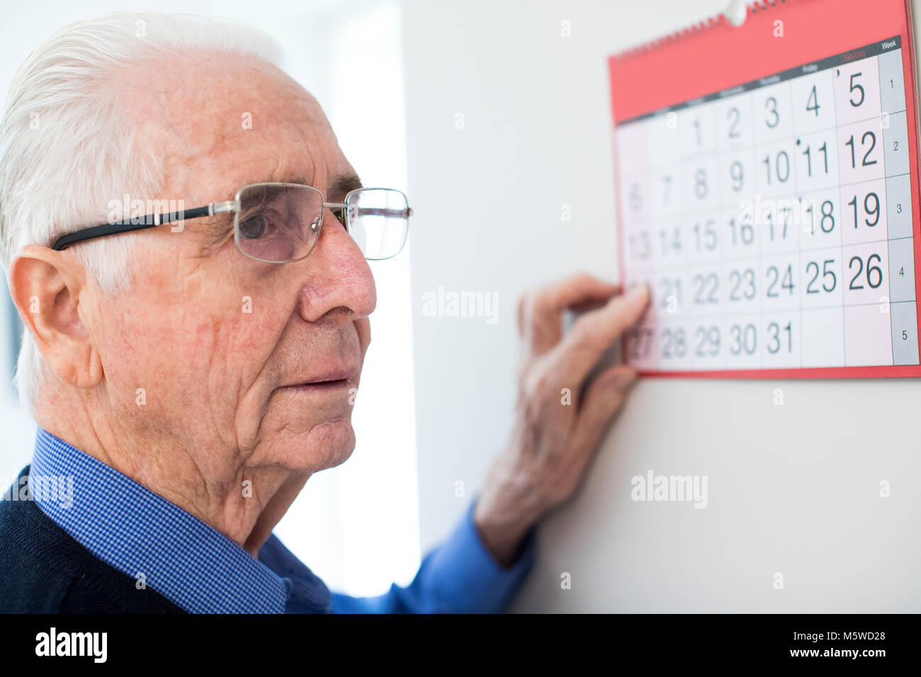Confuso uomo anziano con demenza guardando il calendario da parete Foto Stock