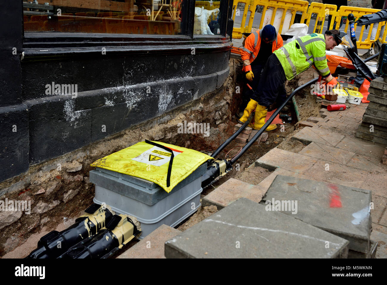 Elettricità workman riparare la rete sotterranea di cavi elettrici in lavorazione foro nella pavimentazione Foto Stock