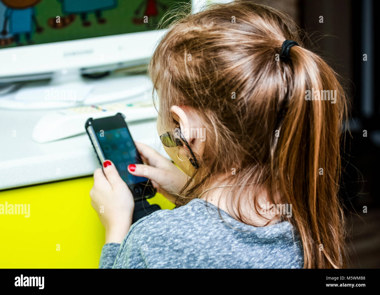 Una bambina con un auricolare wireless nel suo orecchio con entusiasmo è inserita nello smartphone. Foto Stock