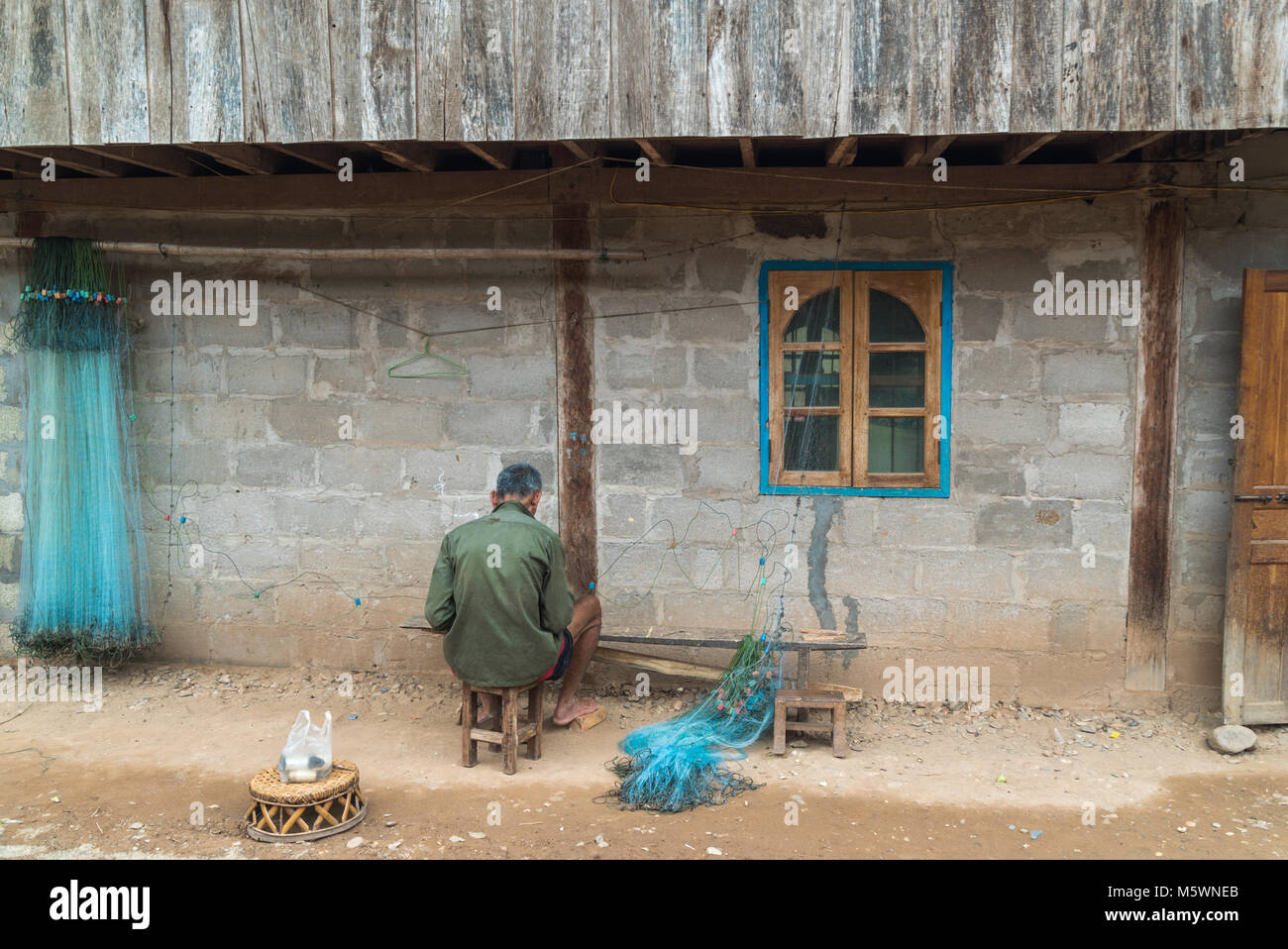 Un Lao Loum uomo etnico dal bellissimo villaggio tribale di Muang Ngoy riparando la sua rete da pesca che sarà successivamente gettato nel fiume Nam Ou. Foto Stock