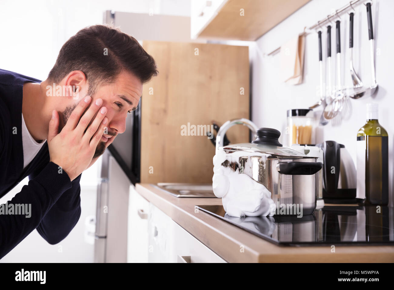 Scioccato giovane uomo guardando la fuoriuscita di latte bollito dall'arnese di cucina Foto Stock