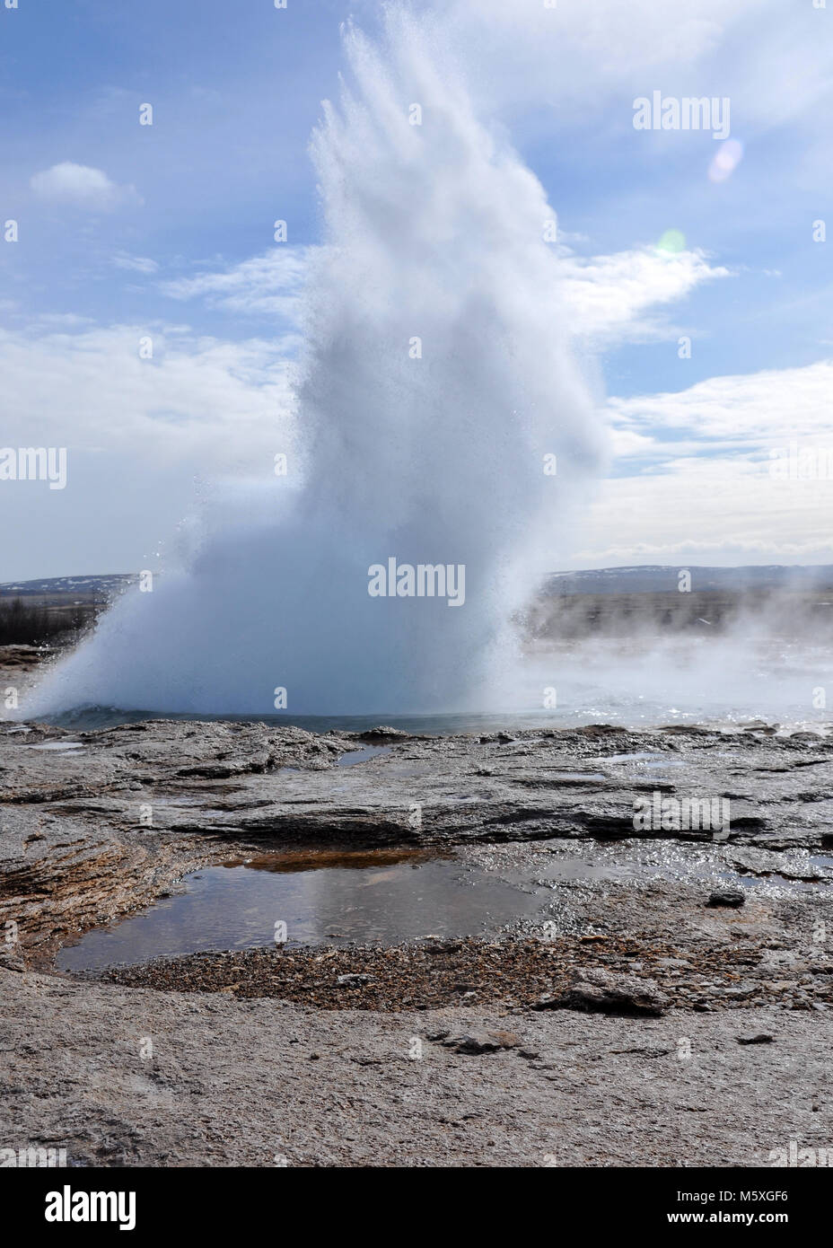 Geyser Strokkur erutting con un sacco di vapore e acqua, Islanda. Rocce e acqua in primo piano. Foto Stock