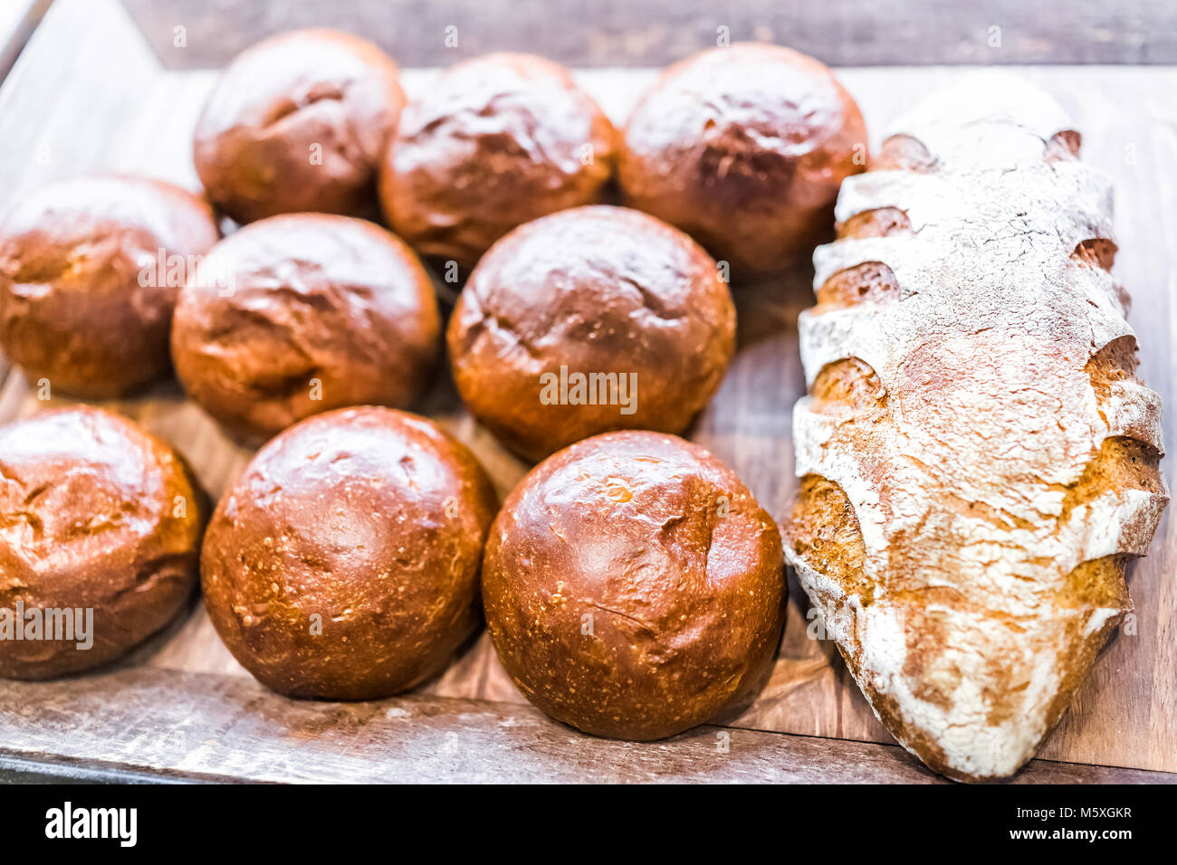 Primo piano della fresca bruna rigata di pasta acida cotta pagnotte di pane in panetteria con molti panini rotoli Foto Stock