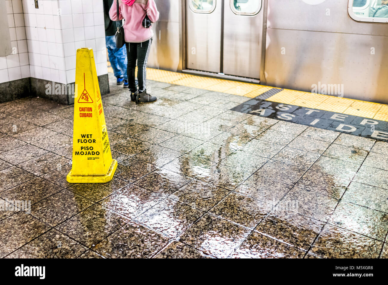 La città di New York, Stati Uniti d'America - 29 Ottobre 2017: Attesa di persone in transito sotterraneo vuoto grande piattaforma in NYC Stazione della Metropolitana, primo piano del pavimento bagnato segno sli Foto Stock