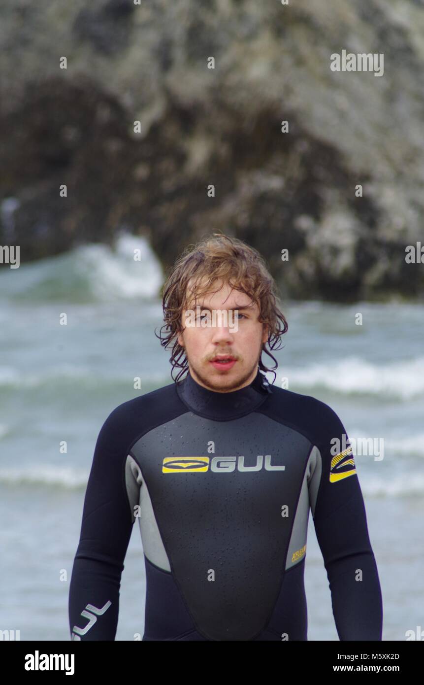 Giovani, resistente bello British Surfer, in una muta sulla spiaggia di Holywell, North Cornwall, Regno Unito. Surf Lifestyle. Foto Stock