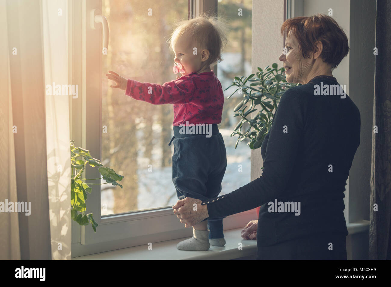 Bambino e nanny di trascorrere del tempo insieme a casa guardando attraverso la finestra Foto Stock