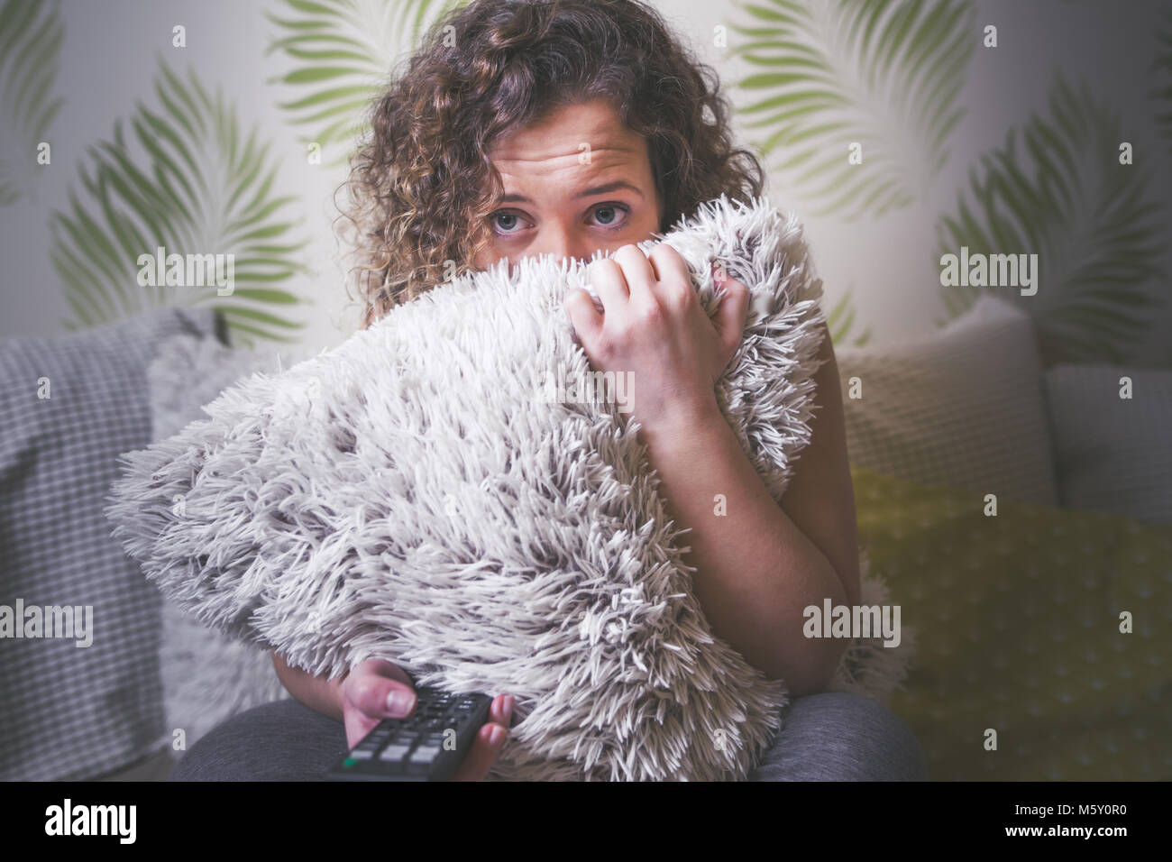 Spaventata giovane donna guardando film horror in TV Foto Stock