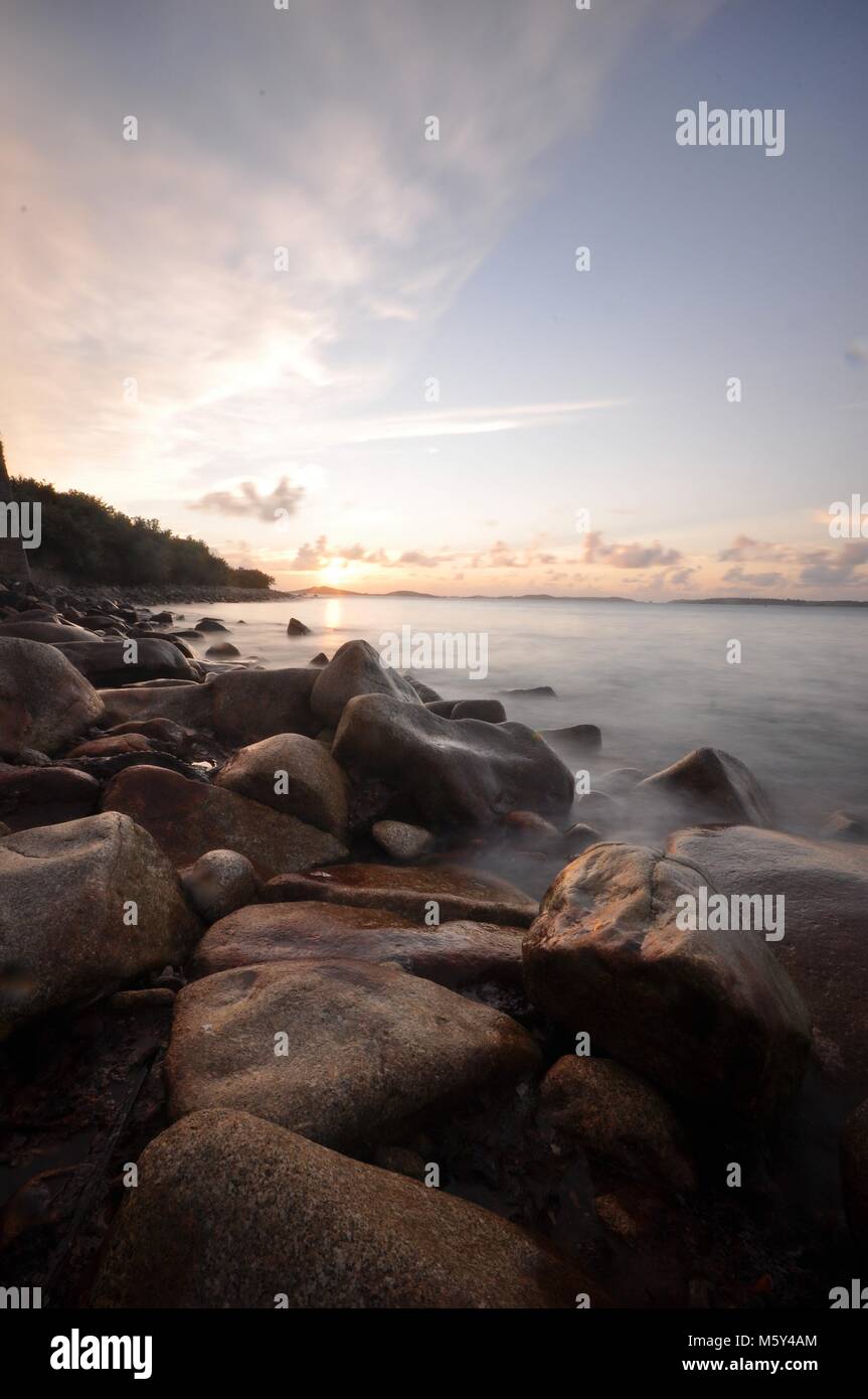 Tramonto sul mare attraverso la costa rocciosa con lunga esposizione e acqua dolce. Isole di Scilly, vista sul mare fino all'isola di Samson al tramonto. Foto Stock