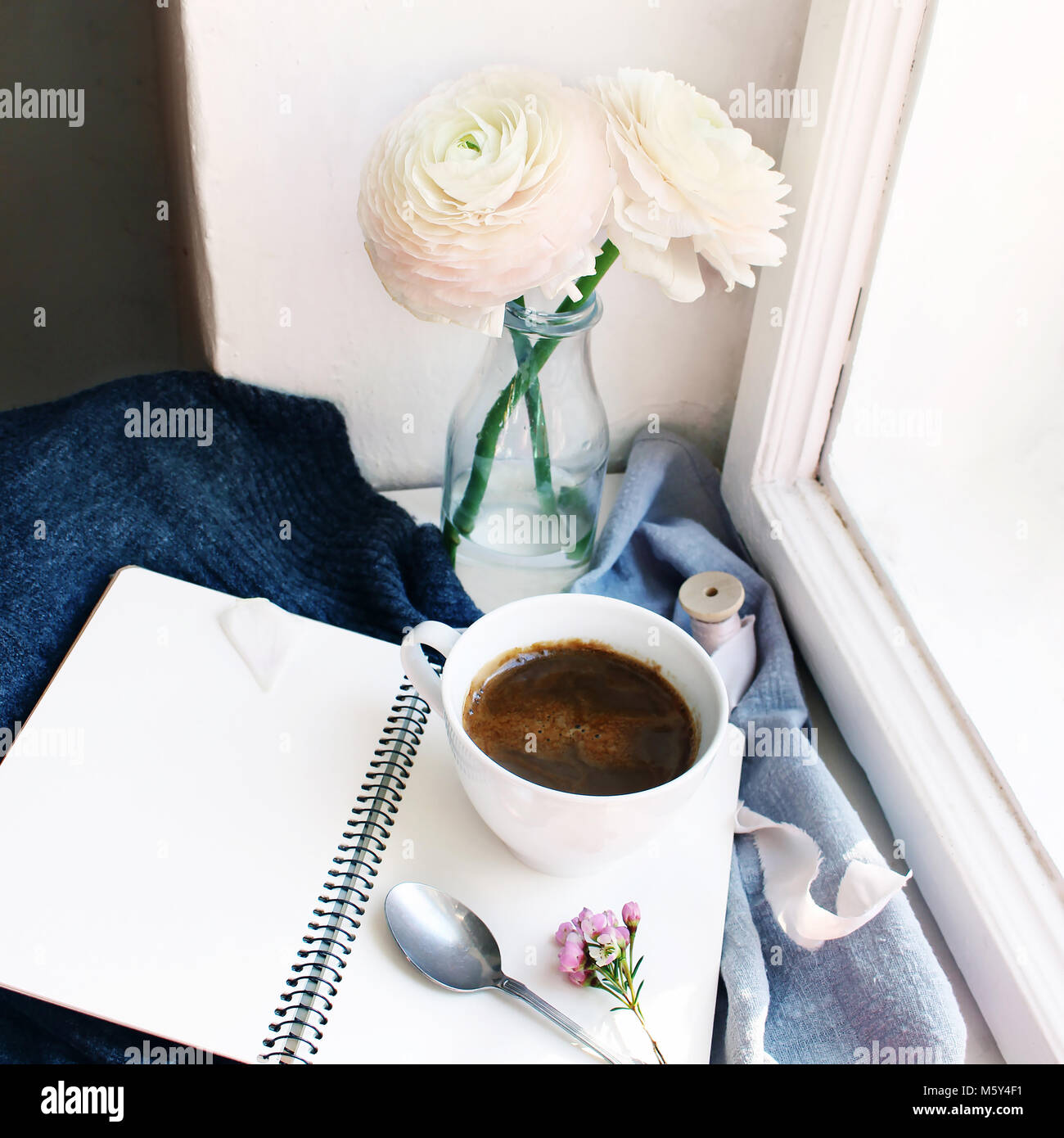 Accogliente la molla ancora in vita. La tazza di caffè caldo, aperto il notebook vuoto con caldi plaid sul davanzale vintage. Stile femminile stock photo, composizione floreale con roselline, ranuncoli fiori. Foto Stock