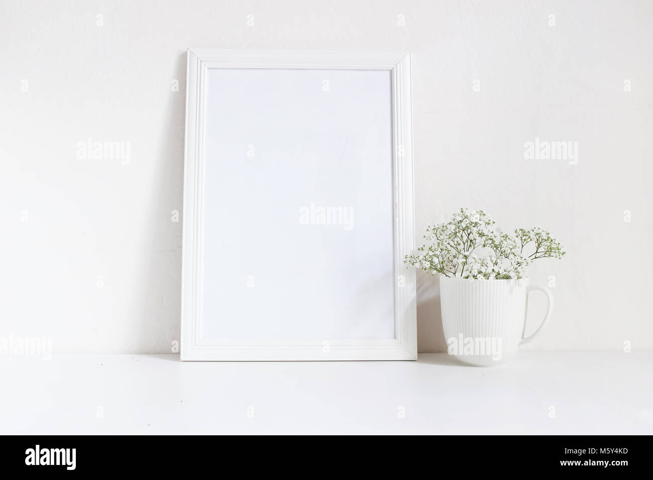 Vuoto bianco telaio in legno mockup con baby soffio, Gypsophila fiori nella tazza di porcellana sul tavolo. Poster design di prodotto. Stile femminile stock photography. Home decor. Foto Stock