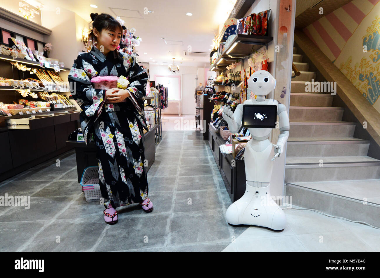 Una donna giapponese vestita in kimono interagente con un robot. Foto Stock
