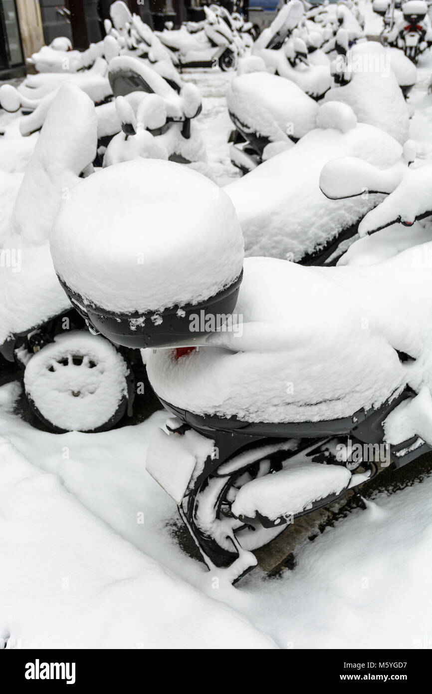 Coperta di neve a due e a tre ruote scooter con top casi parcheggiato all'aperto per le strade di Parigi in un giorno d'inverno. Foto Stock