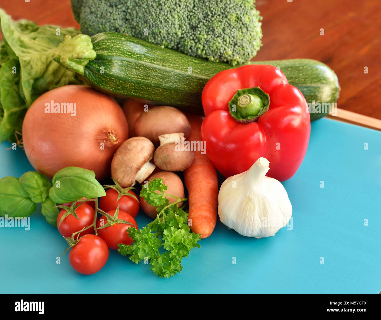 Fresche verdure crude su un tagliere. disposizione di peperone rosso, zucchine, broccoli, insalata, cipolla, carote e aglio, decorate in bambù. Foto Stock
