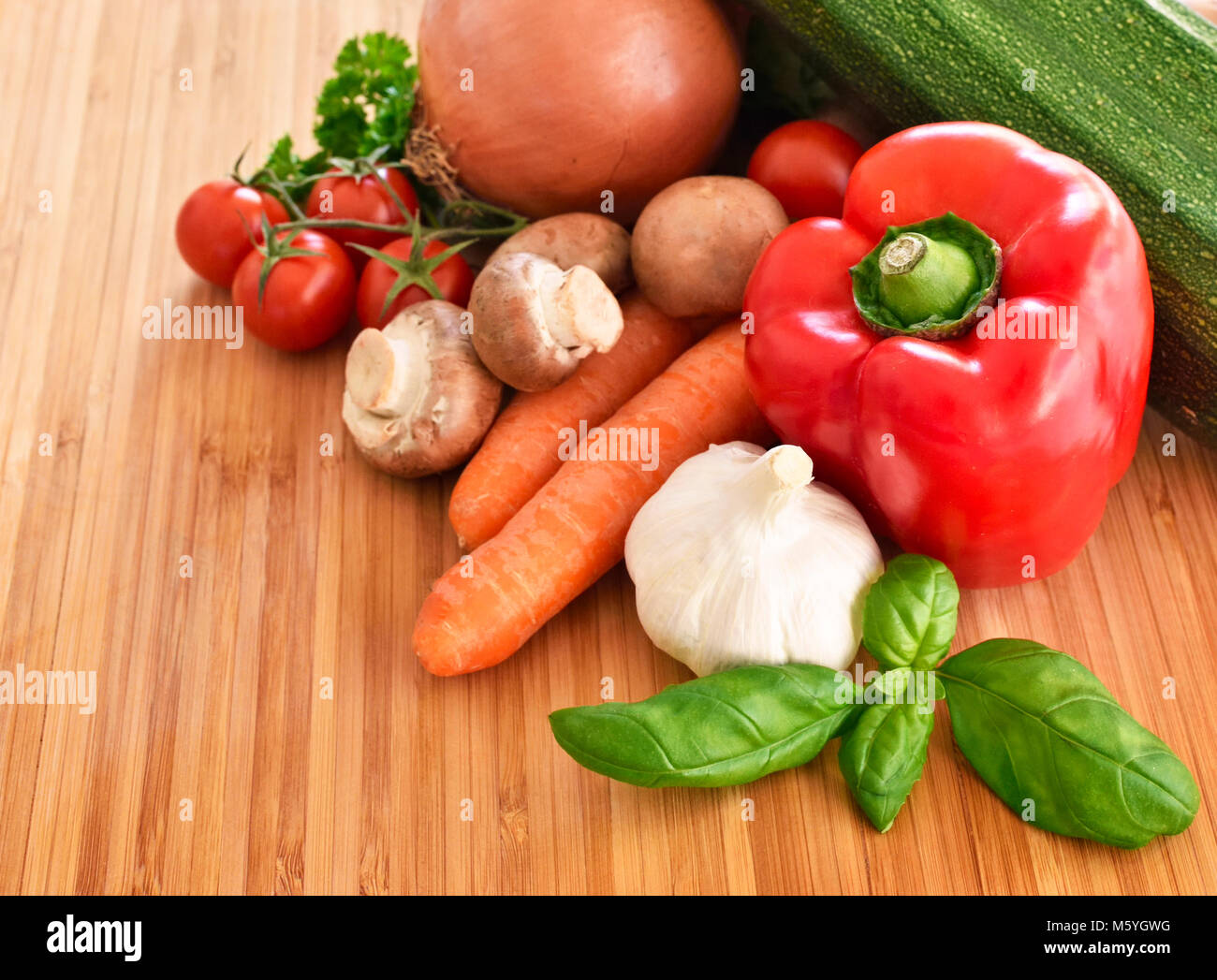 Fresche verdure crude su un tagliere. disposizione di peperone rosso, zucchine, broccoli, insalata, cipolla, carote e aglio, decorate in bambù. Foto Stock