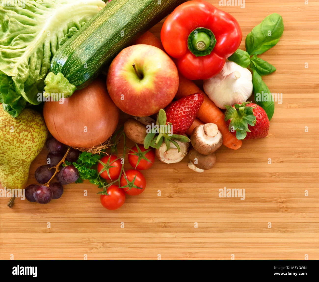 La verdura e la frutta composizione o la disposizione su un bambù tagliere. I prodotti freschi, il peperone rosso, Apple, carote, cipolle, aglio, fragola Foto Stock
