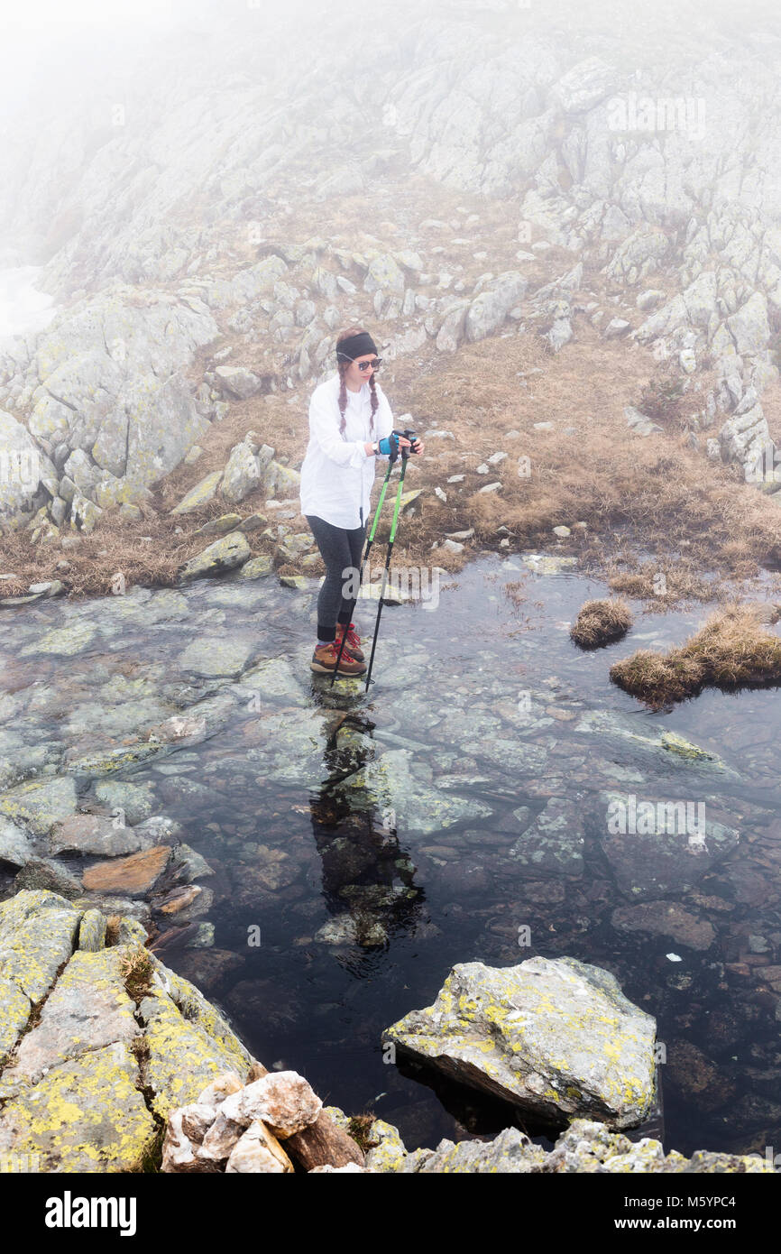 Giovane donna di viaggiatori una passeggiata attraversa il fiume, godendo di un incredibile a piedi, passeggiare ed esplorare la natura. Ragazza turistica hipster sullo sfondo del paesaggio della valle. Foto Stock