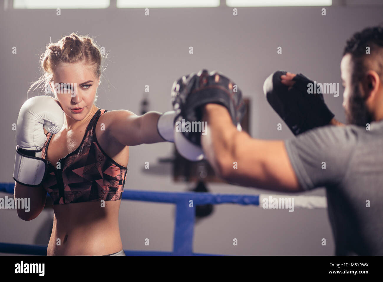 Ragazza boxing training su guanti da boxe detenute da un boxer master Foto Stock