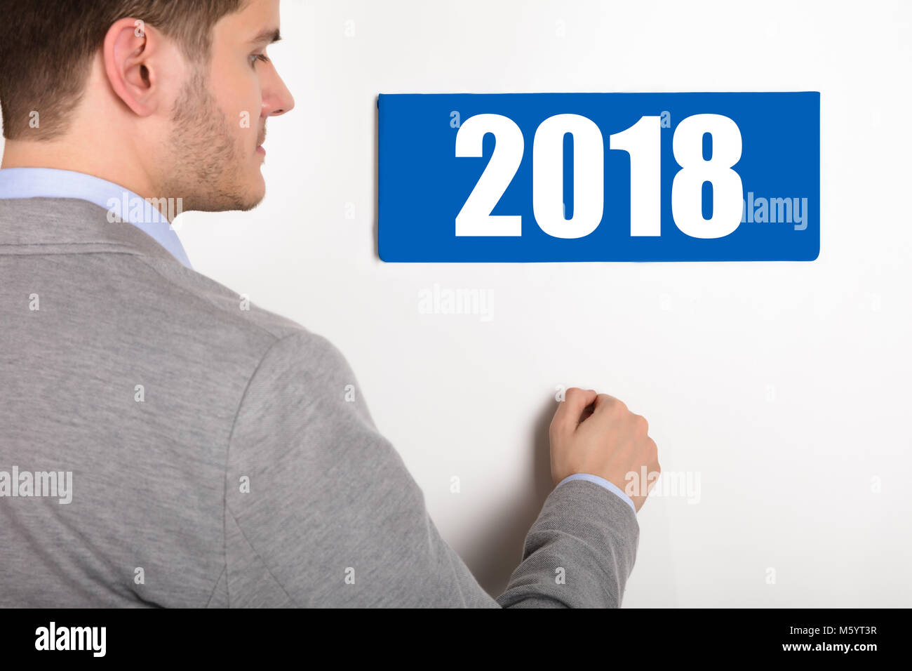 Close-up di un giovane imprenditore a bussare porta bianca con 2018 indicati sulla targhetta Foto Stock