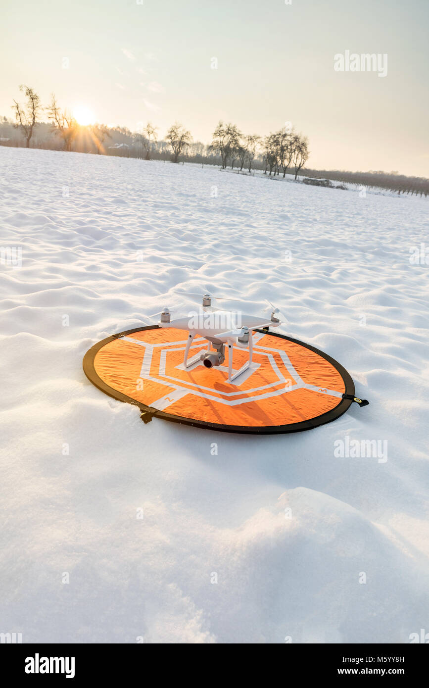 Foto di un bianco quadcopter professionale drone permanente della telecamera su un eliporto con il bianco della neve in inverno nella parte anteriore della foresta Foto Stock