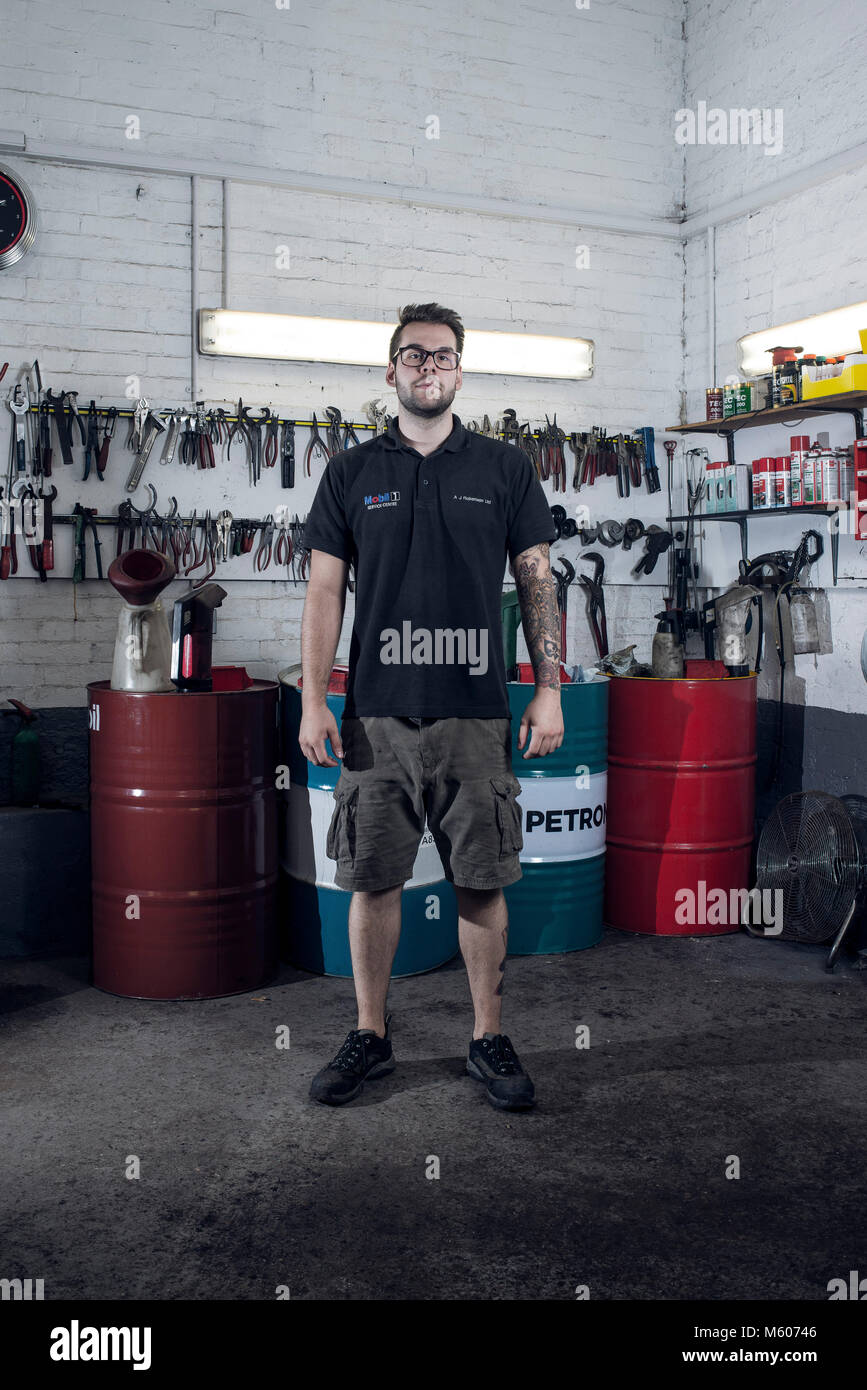 Locali di proprietari di piccole aziende meccanica posare per un ritratto sul pavimento del garage di fronte ai loro strumenti Foto Stock