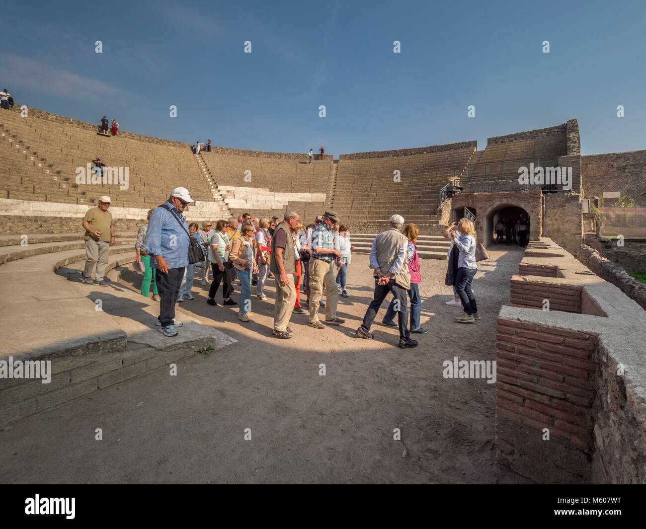 I turisti al cavae (area salotto del pubblico) parte del grande Teatro scavato dalle rovine della città di Pompei, Italia. Foto Stock