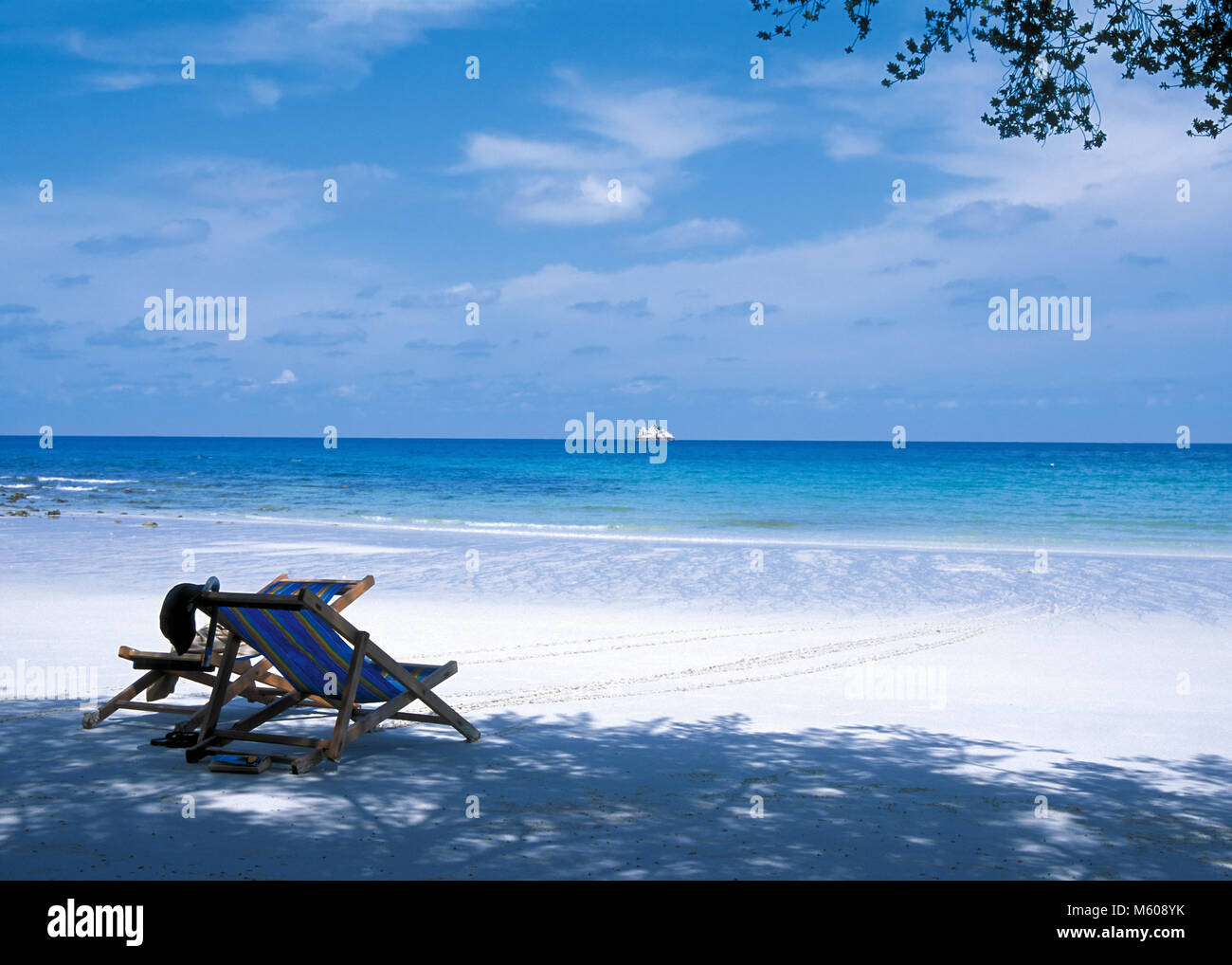 Due di legno chaise-longue sulla bianca spiaggia tropicale contro il calmo mare blu Foto Stock