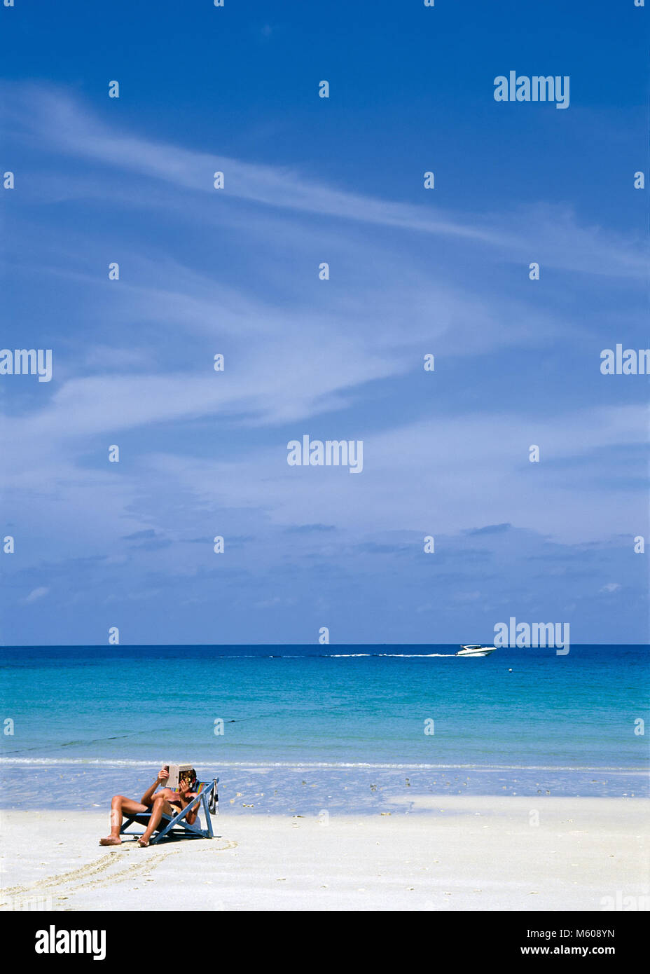 La singola persona che stabilisce nel lettino la lettura di un libro su una spiaggia bianca contro il mare tropicale Foto Stock