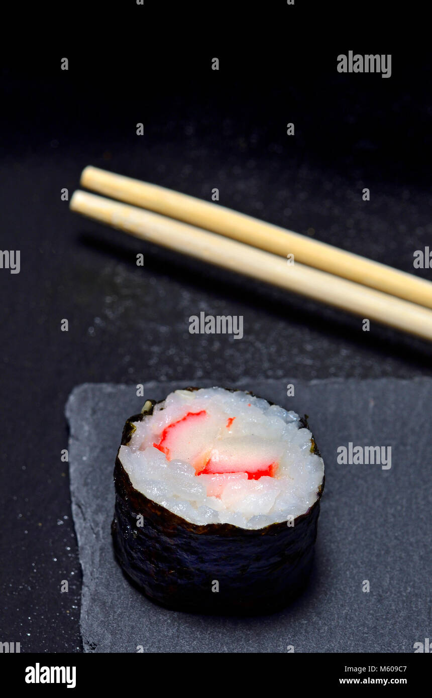 Sushi su una piastra di ardesia: maki (rotolo avvolto in alghe marine) e bastoncini Foto Stock