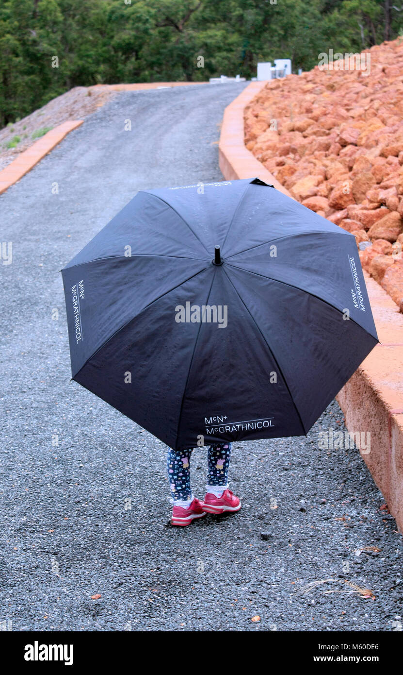 Un giovane bambino si ripara dalla pioggia sotto un ombrello nero Foto  stock - Alamy