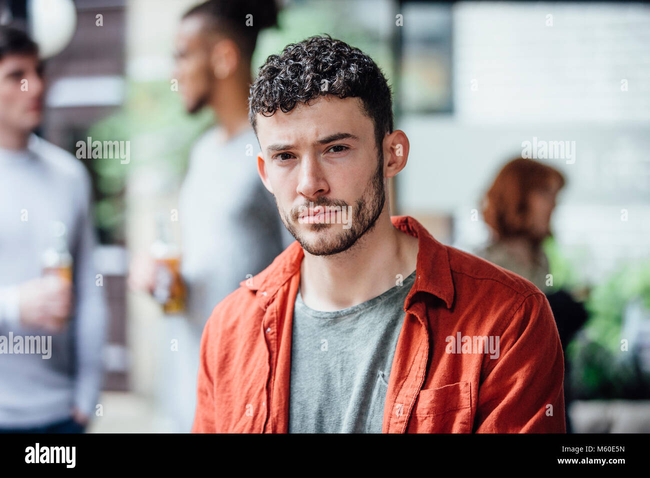 L uomo è guardando la telecamera con un look pensieroso mentre in una riunione sociale in un bar cortile. Foto Stock