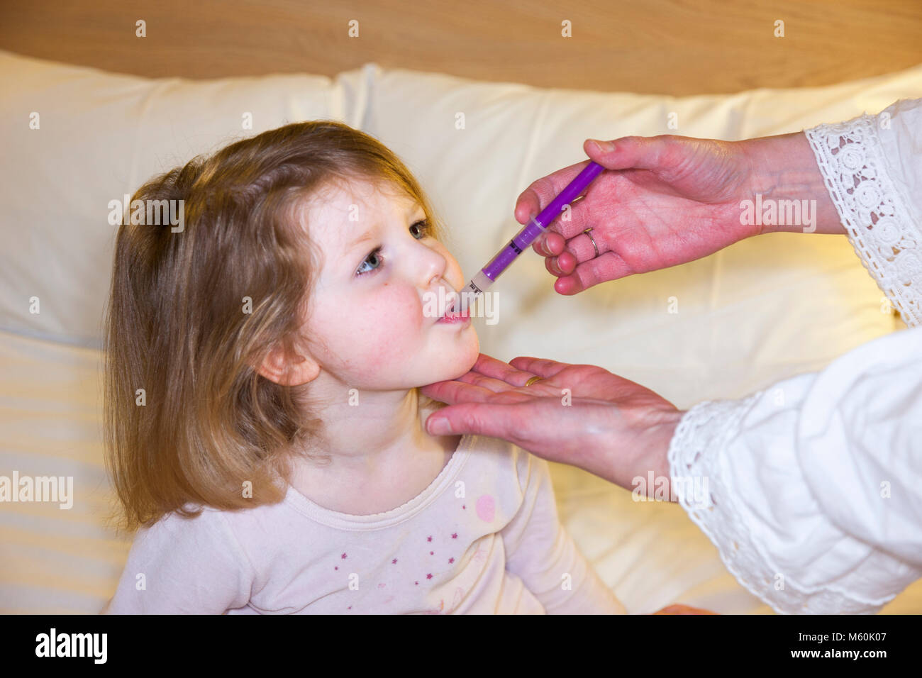 Madre / mamma / mom dando Calpol medicina con paracetamolo per - apparentemente - malati / ill bambino / bambino / ragazza a letto con la febbre o la temperatura. (95) Foto Stock