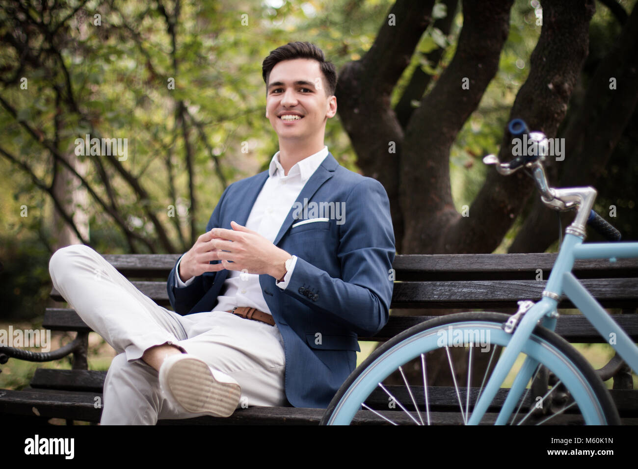 Giovane imprenditore attraente e seduta in attesa su una panchina nel parco con la sua bicicletta accanto a lui Foto Stock