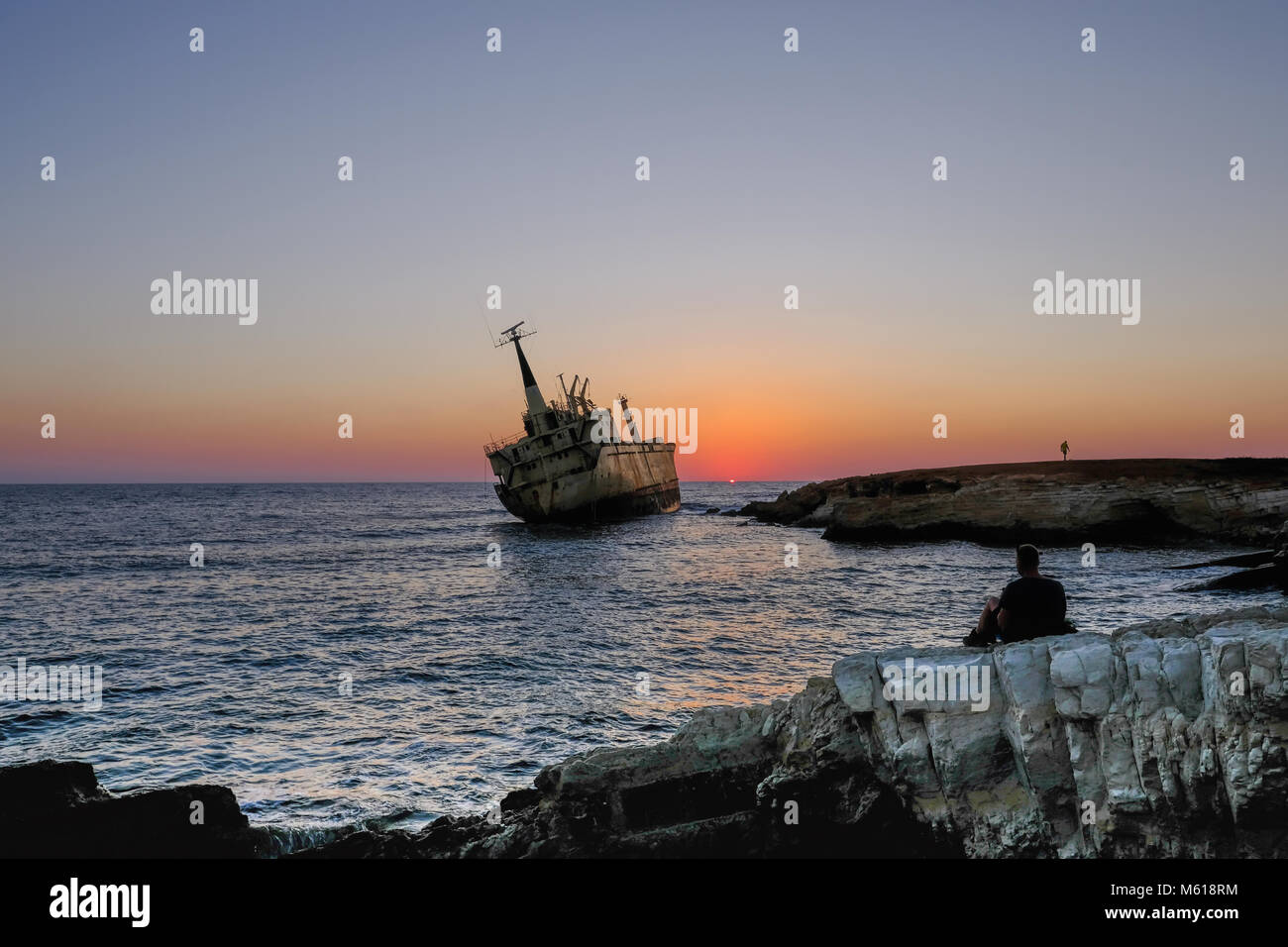 Uomo seduto a guardare il tramonto sul punto di riferimento naufragio a Pafos, Cipro. Foto Stock
