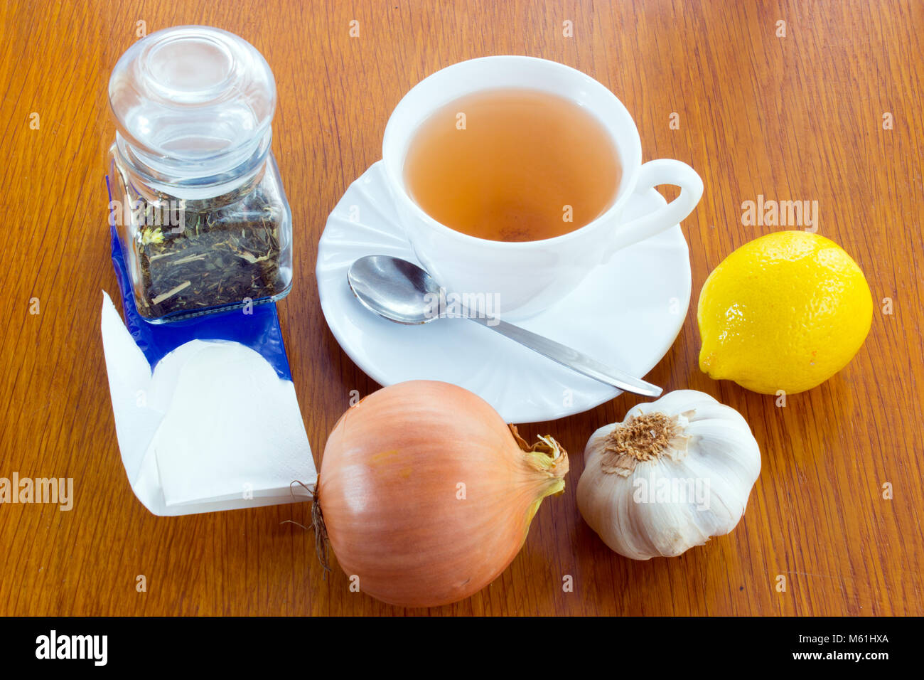 Una tazza di tè con piattino e cucchiaio, limone, cipolla, aglio, una dose di vetro con tè, fazzoletti di carta. Tutto contro di prendere freddo sul legno de Foto Stock