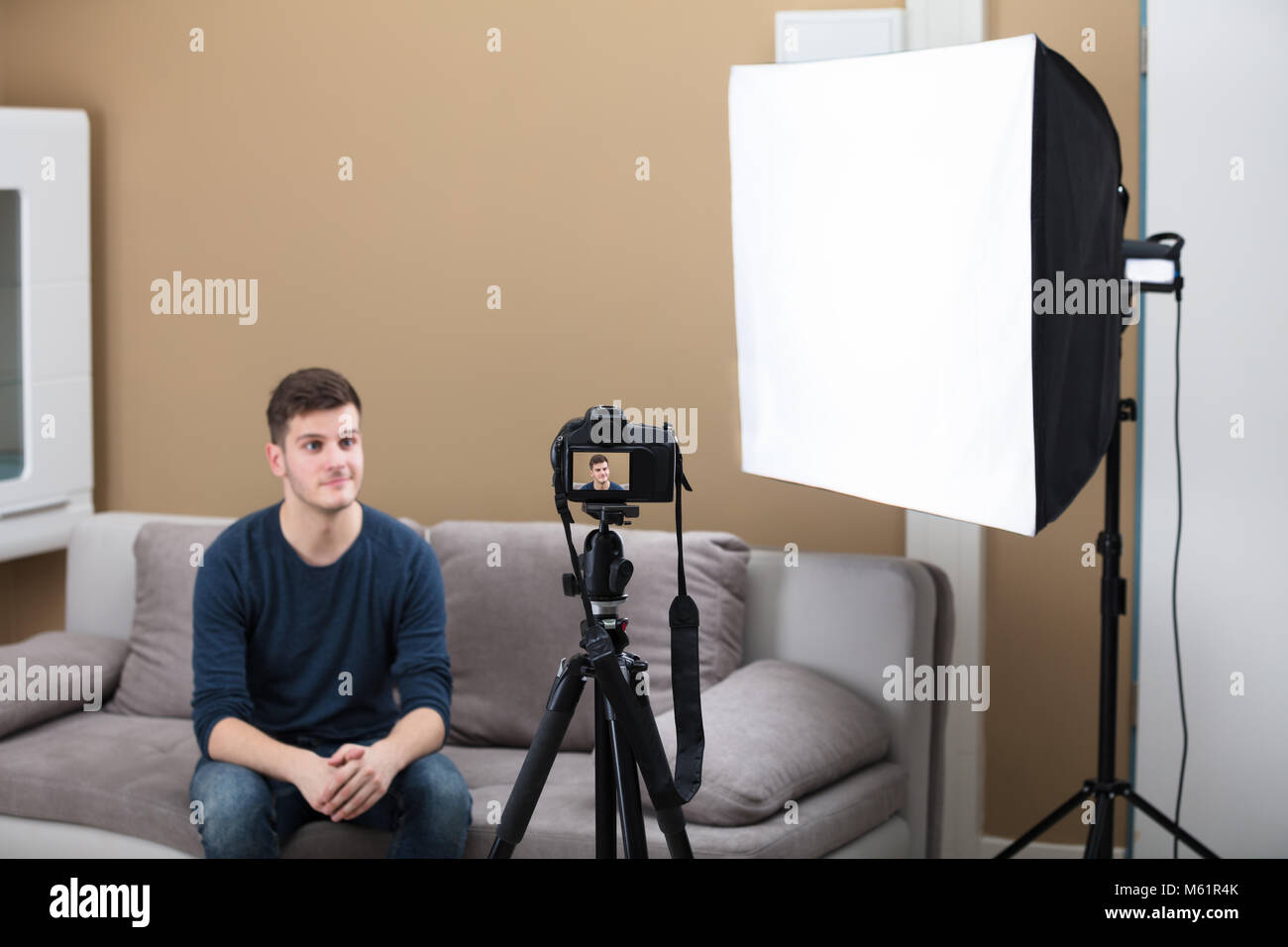 Giovane Maschio Blogger seduto sul divano la registrazione di un video con la fotocamera a casa Foto Stock