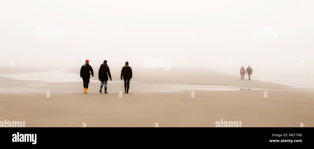 3 persone a piedi, spiaggia nebbiosa, stazione balneare, San Pietro Ording, Germania. Nelle maree, l'acqua scorre verso il mare con bassa marea e nell'altra direzione con alta marea. Nella nebbia, il Mar di Wadden può diventare un labirinto Foto Stock