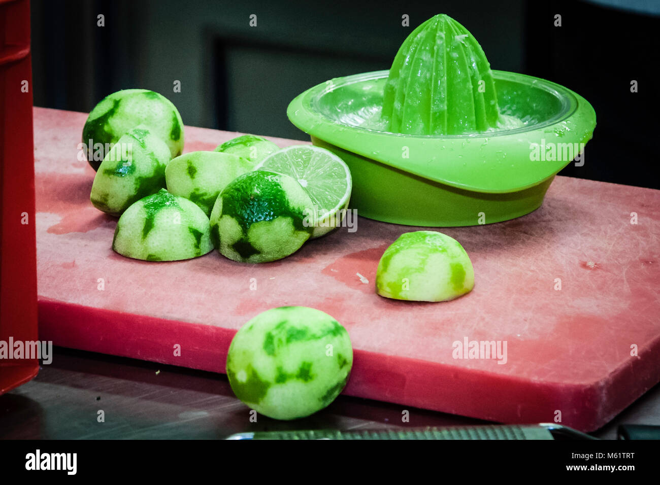 La freschezza è la carta vincente. La buccia e il succo di lime sostengono il cibo fresco regionale con il loro aroma. Calce verde schiacciata e uno spremiagrumi verde su un tagliere rosso Foto Stock