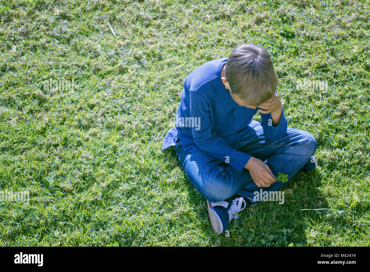 Infelice triste sconvolto ragazzo seduto da solo sull'erba Foto Stock