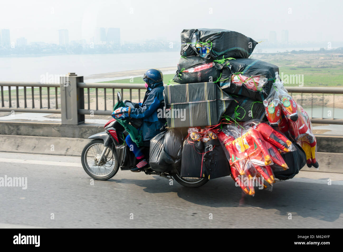 Una persona che cavalca un scooter con un carico molto pesante delle merci,  comunemente visto in Vietnam Foto stock - Alamy