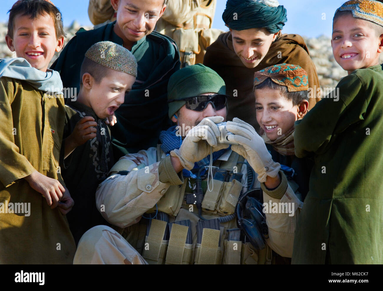 Un soldato americano mostra i bambini afghani foto di se stessi che egli ha preso di loro Foto Stock