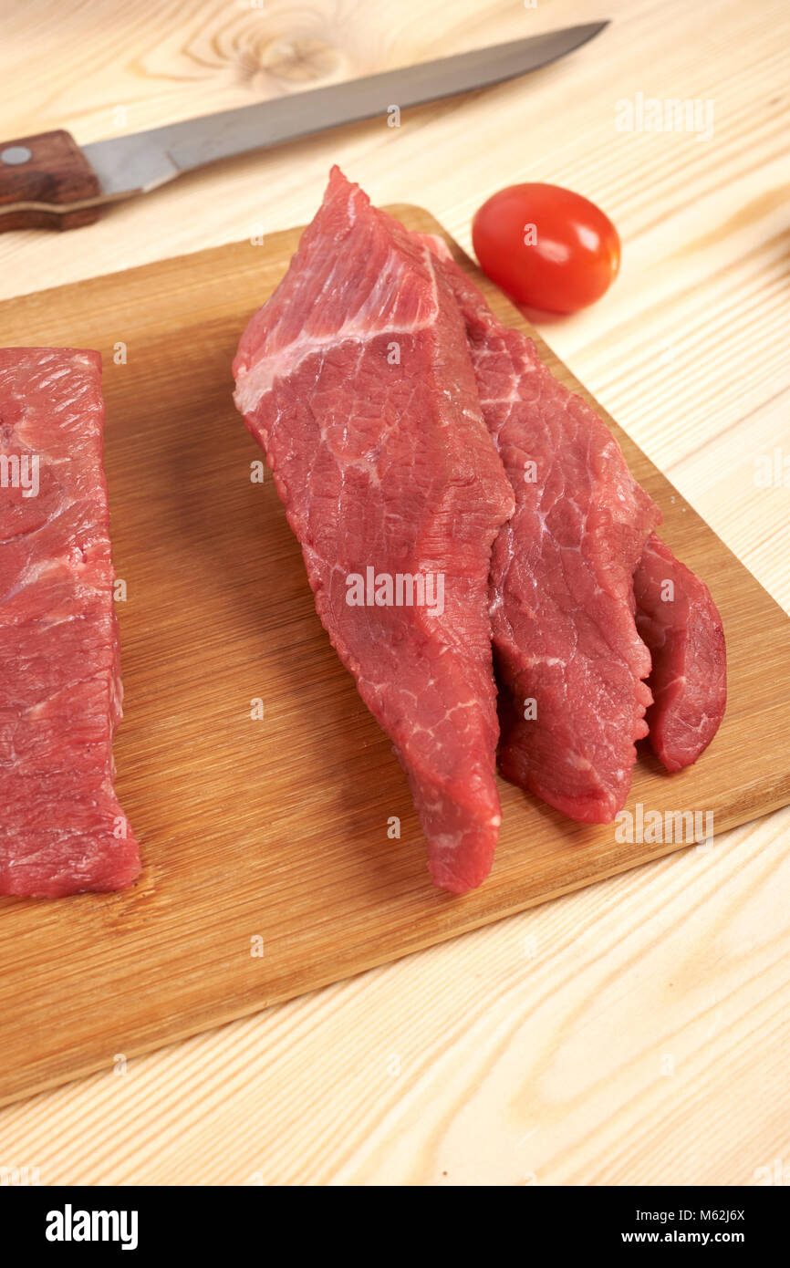 Fette di carne di manzo crudo sul tagliere e verdure Foto Stock