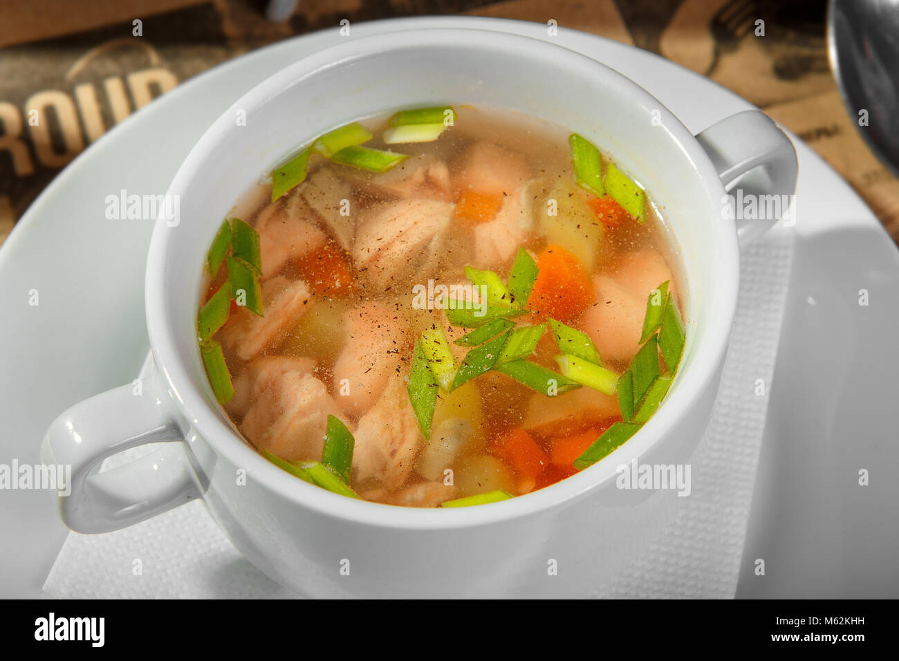 Trasparente con zuppa di pollo, pesce le carote e le erbe e pepe nero macinato, in un profondo piastra bianca. Deposito di un ristorante, bar, cafe. Luce, a basso calo Foto Stock