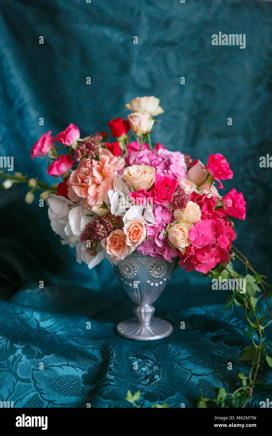 Un bouquet asimmetrico in un vaso di rose, garofani e ortensie su uno sfondo blu scuro Foto Stock