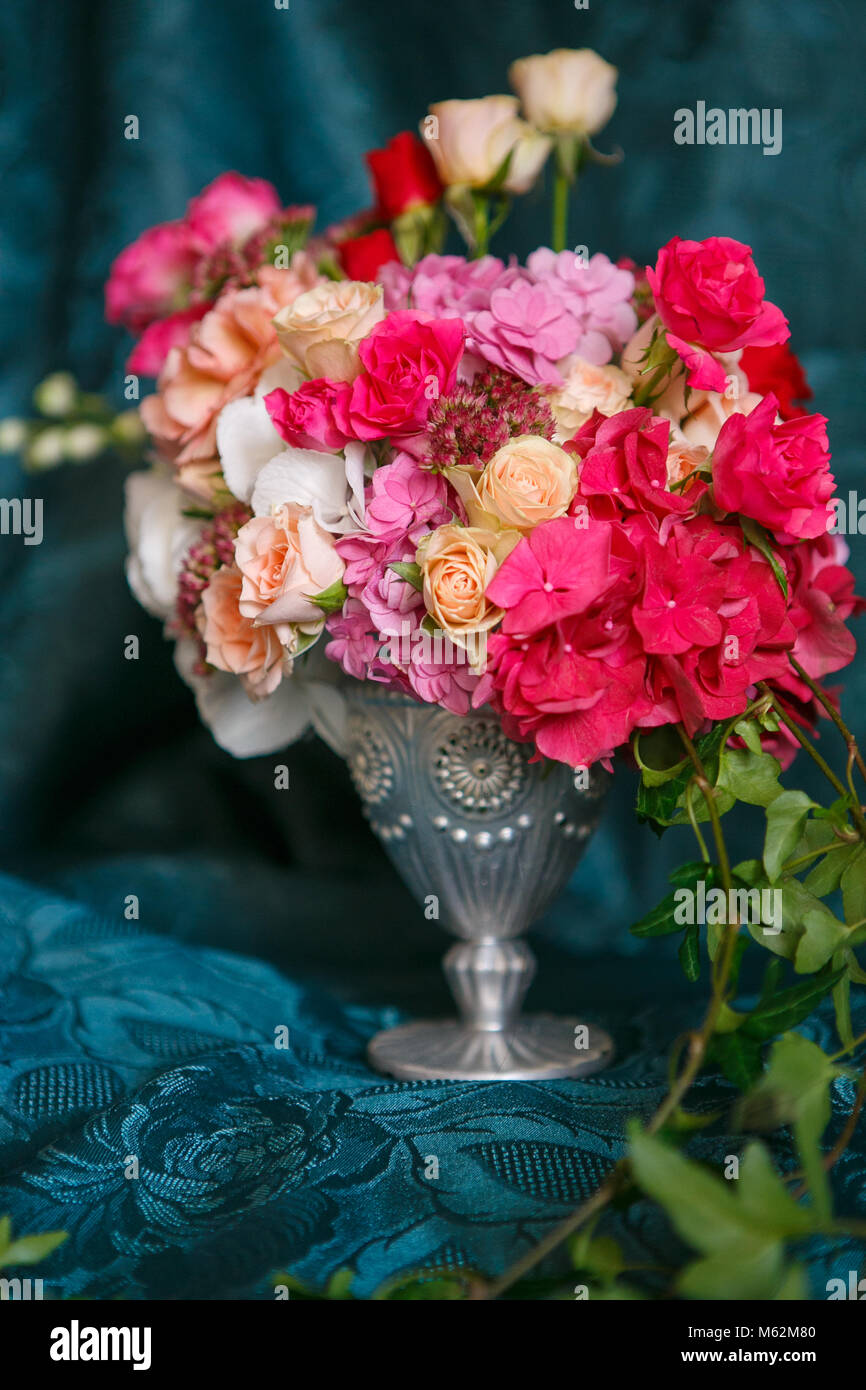 Un bouquet asimmetrico in un vaso di rose, garofani e ortensie su uno sfondo blu scuro Foto Stock