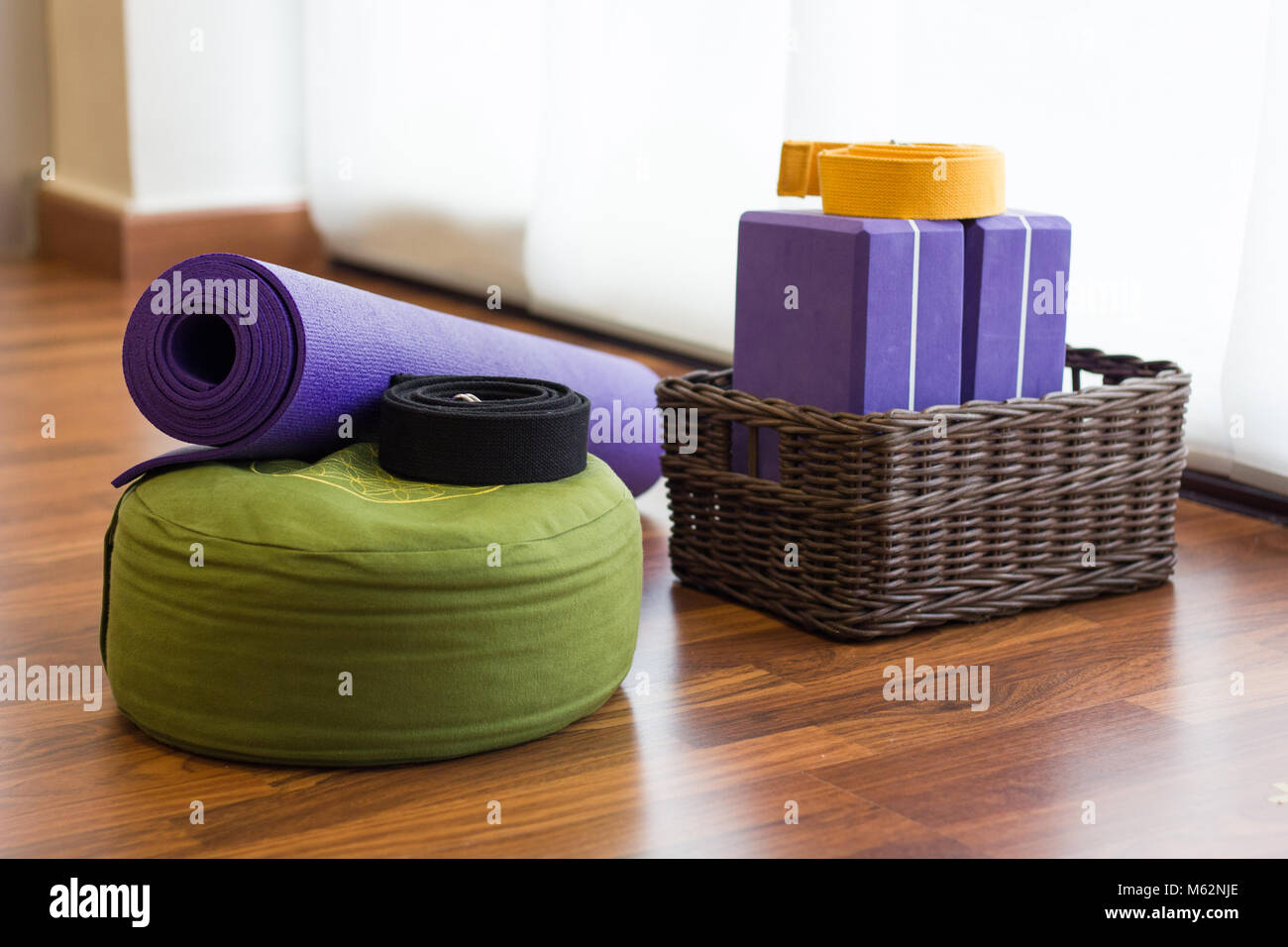 Vari i sostegni di yoga studio sul pavimento di legno. Set di blocchi in cesto in vimini, cinghie, tappetino e cuscino verde nel centro yoga. Wellness nozione di attività Foto Stock