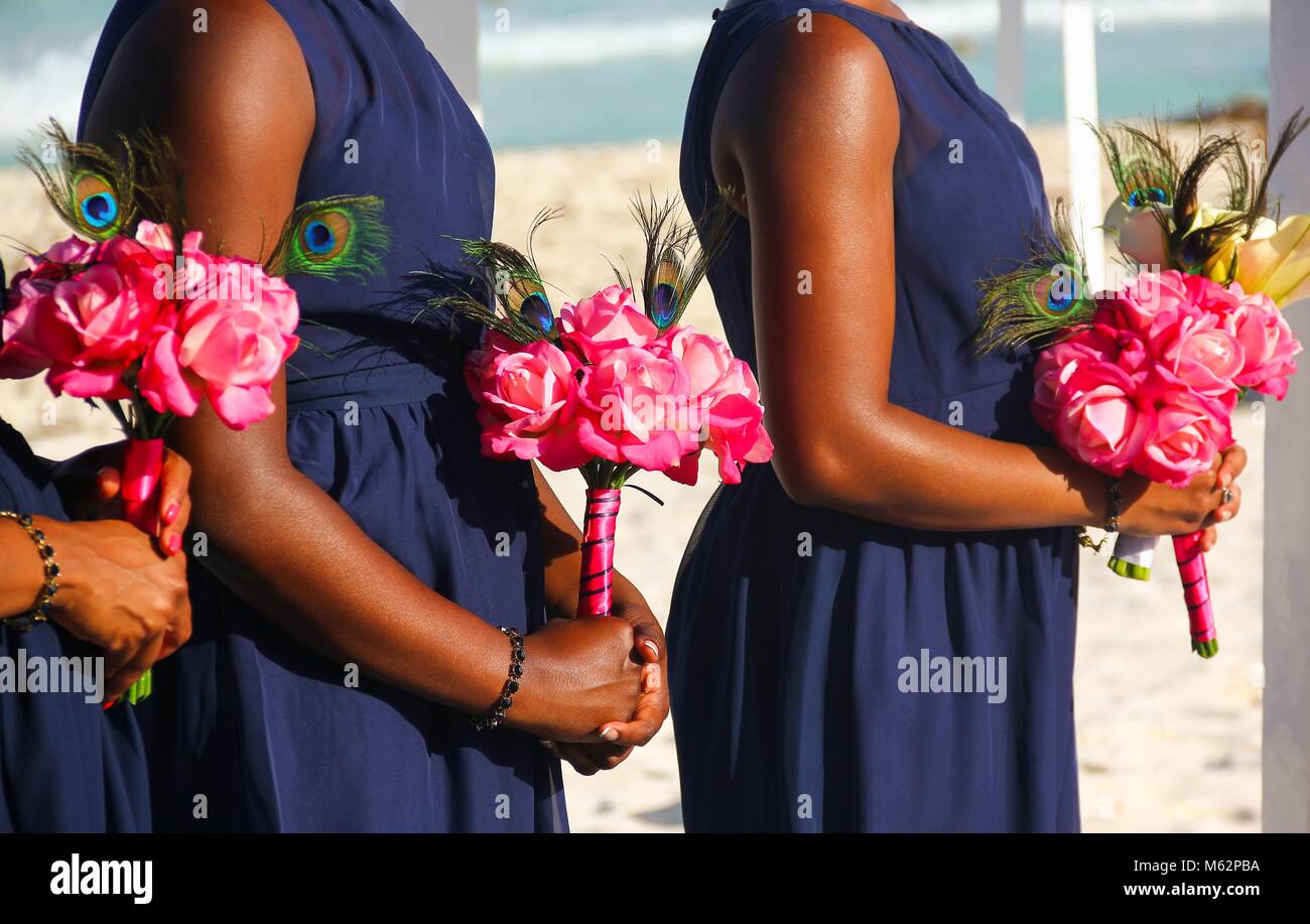 Tre damigelle in blu scuro abito azienda mazzi di fiori di colore rosa ad un matrimonio sulla spiaggia di Cancun, Messico. Americano africano concetto cerimonia Foto Stock
