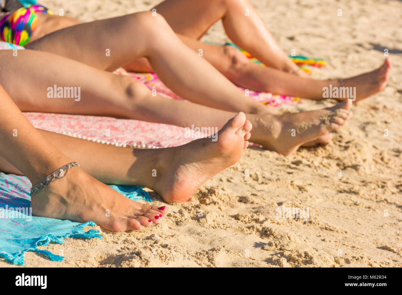 Piedi e gambe di tre donne a prendere il sole sulla spiaggia dell'isola di Koh Phangan, Thailandia. Protezione contro il sole, le vacanze estive, il concetto di tempo libero Foto Stock