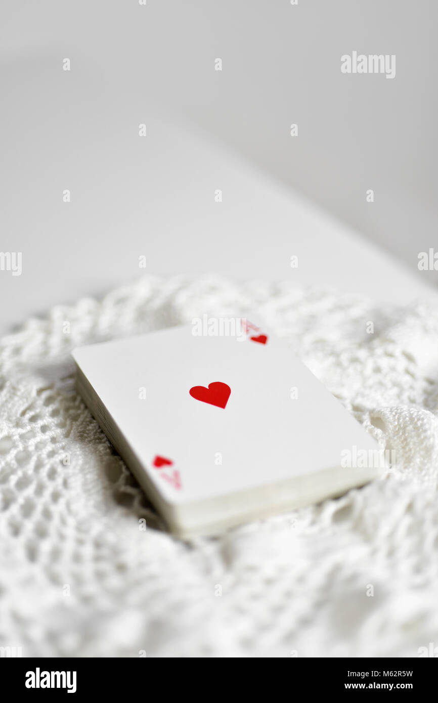 Un mazzo di carte da poker con l'asso di cuori sulla parte superiore, su un centrino a crochet, collocato su un tavolo bianco, con un po' di spazio vuoto sulla parte superiore Foto Stock
